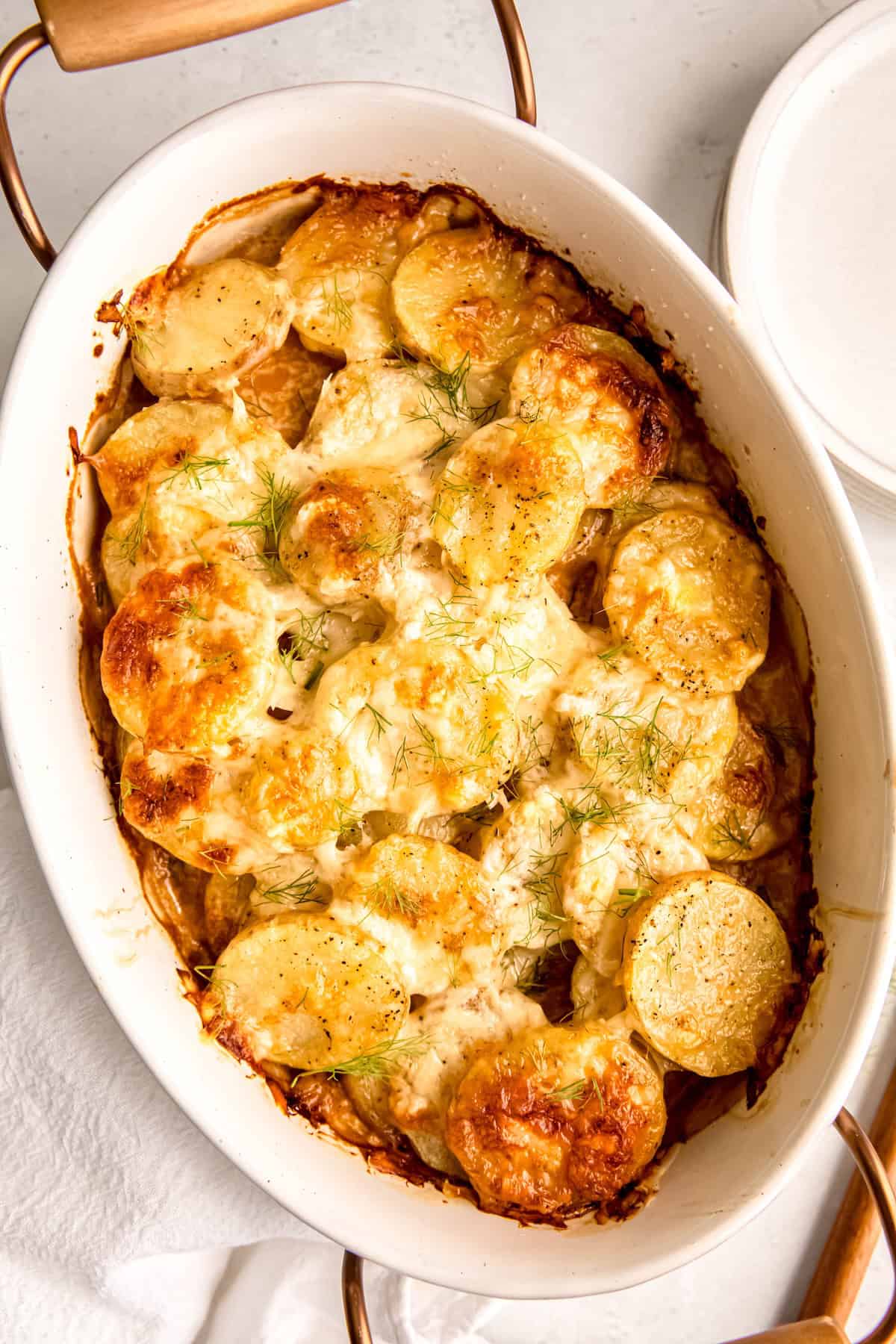 overhead shot of a white oval casserole dish with metal and wooden handles filled with fennel potatoes au gratin.