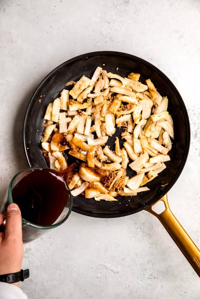 action shot of broth being poured into the skillet with the garlic fennel mixture.