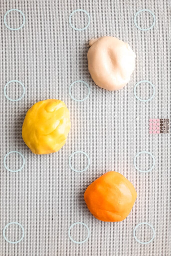 homemade candy corn dough divided into three pieces; one is still white, one is yellow and one is orange after kneading in the food coloring.