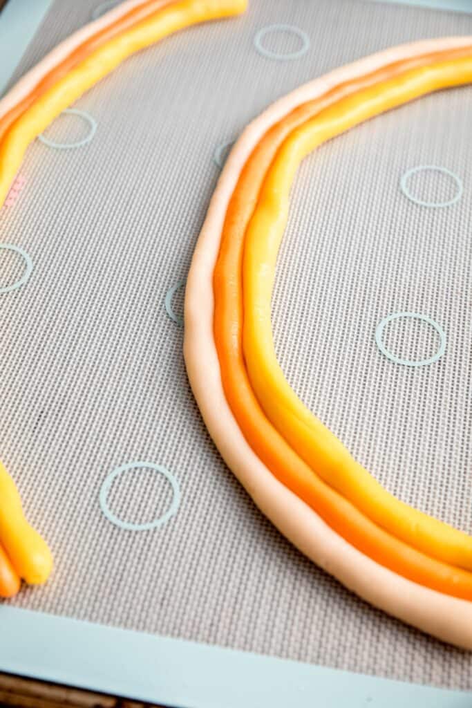 ropes of colored candy corn dough arranged to make 2 "rainbows" of white, orange, and yellow.