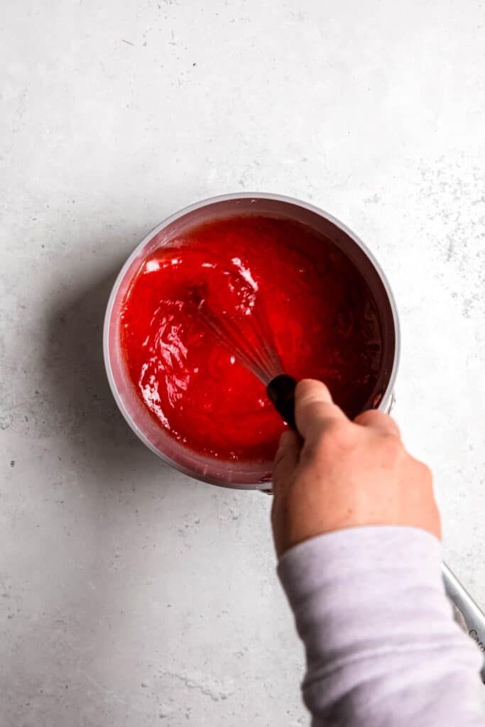 action shot of a hand stirring the jello-cannabis oil mixture for making the gummy mixture.