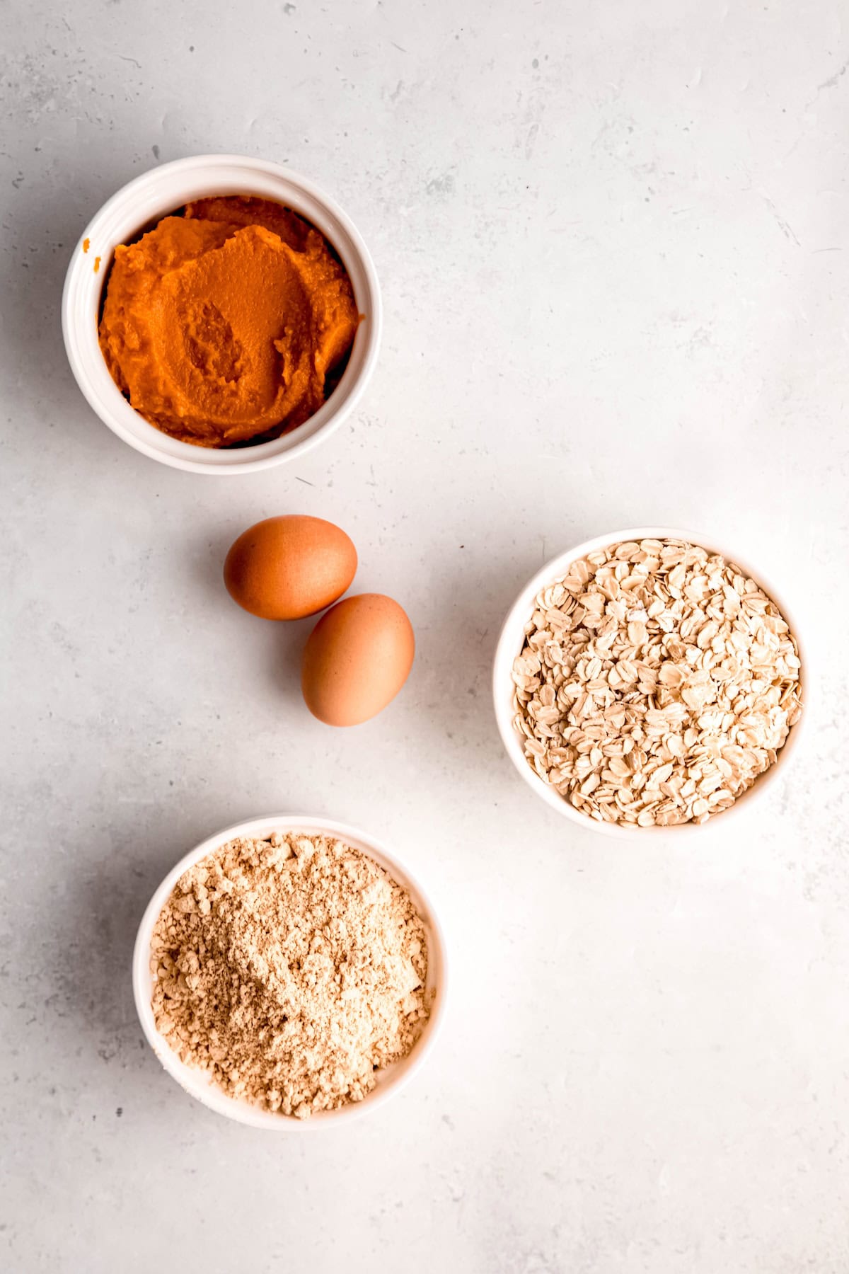 ingredients needed to make dog treats with pumpkin and peanut butter measured out on a white table.
