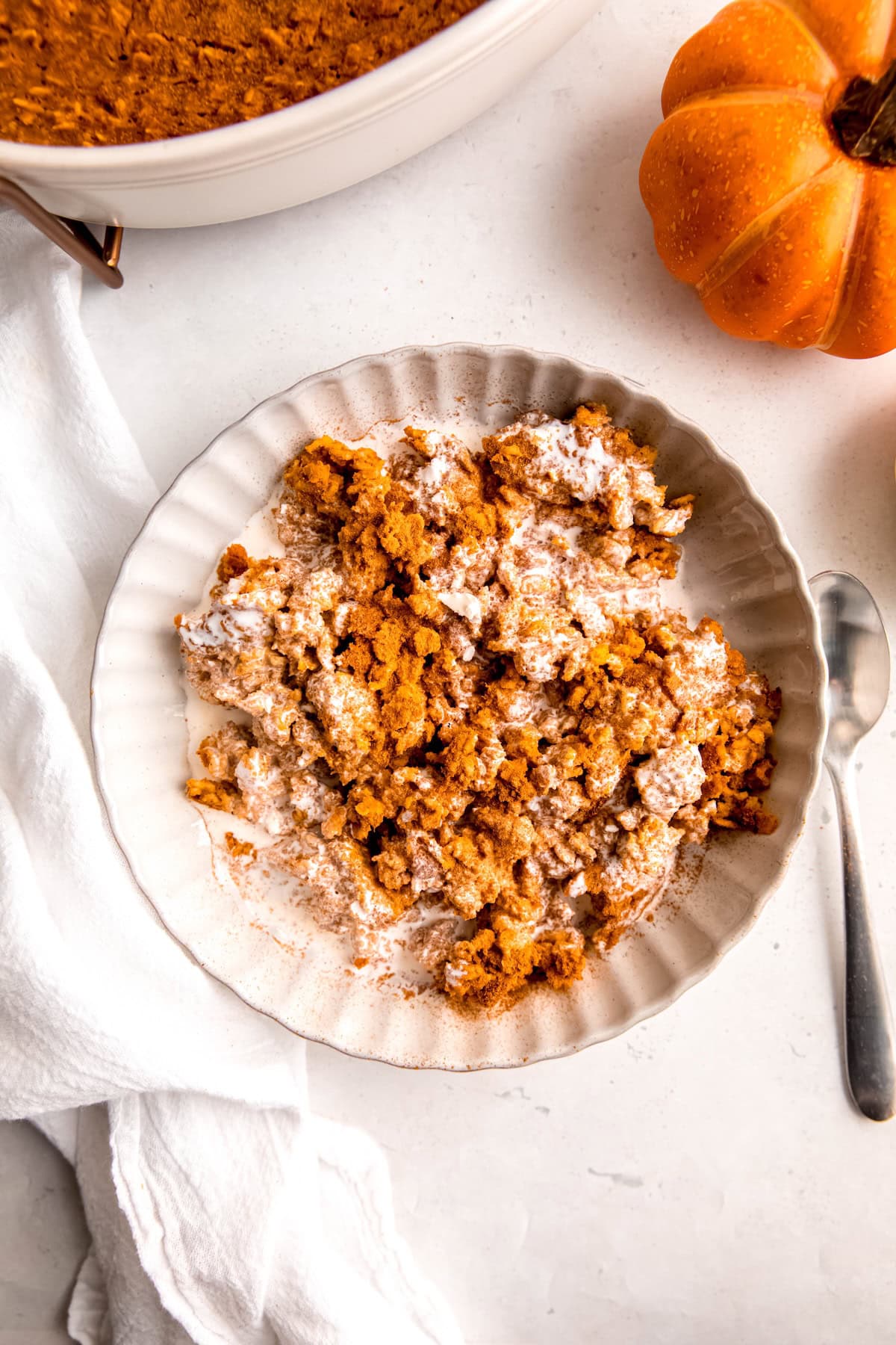 cozy bowl of pumpkin pie baked oatmeal in a white bowl on a white table, with a sivler spoon and an orange mini pumpkin.