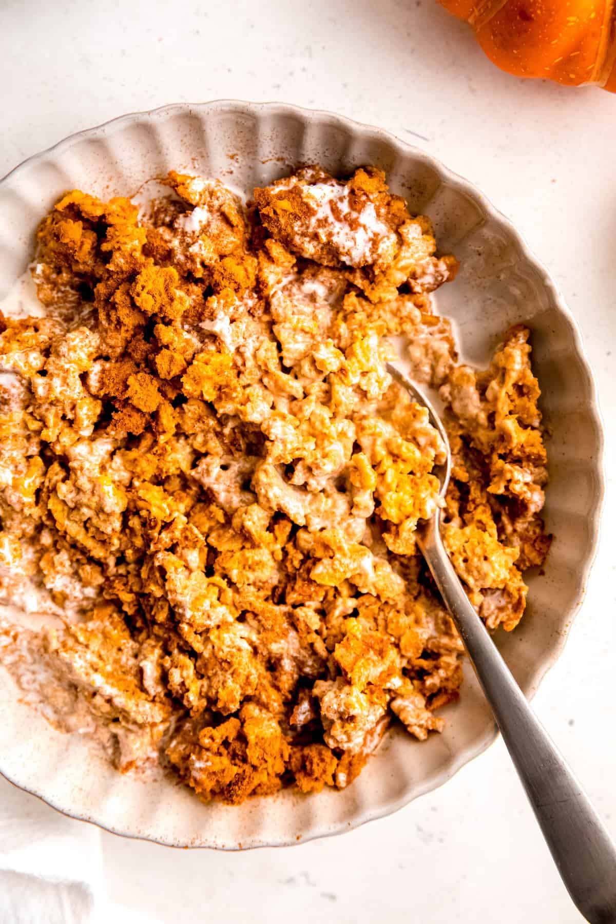 closeup overhead shot of a bowl of pumpkin pie baked oats topped with a drizzle of cream and some cinnamon.