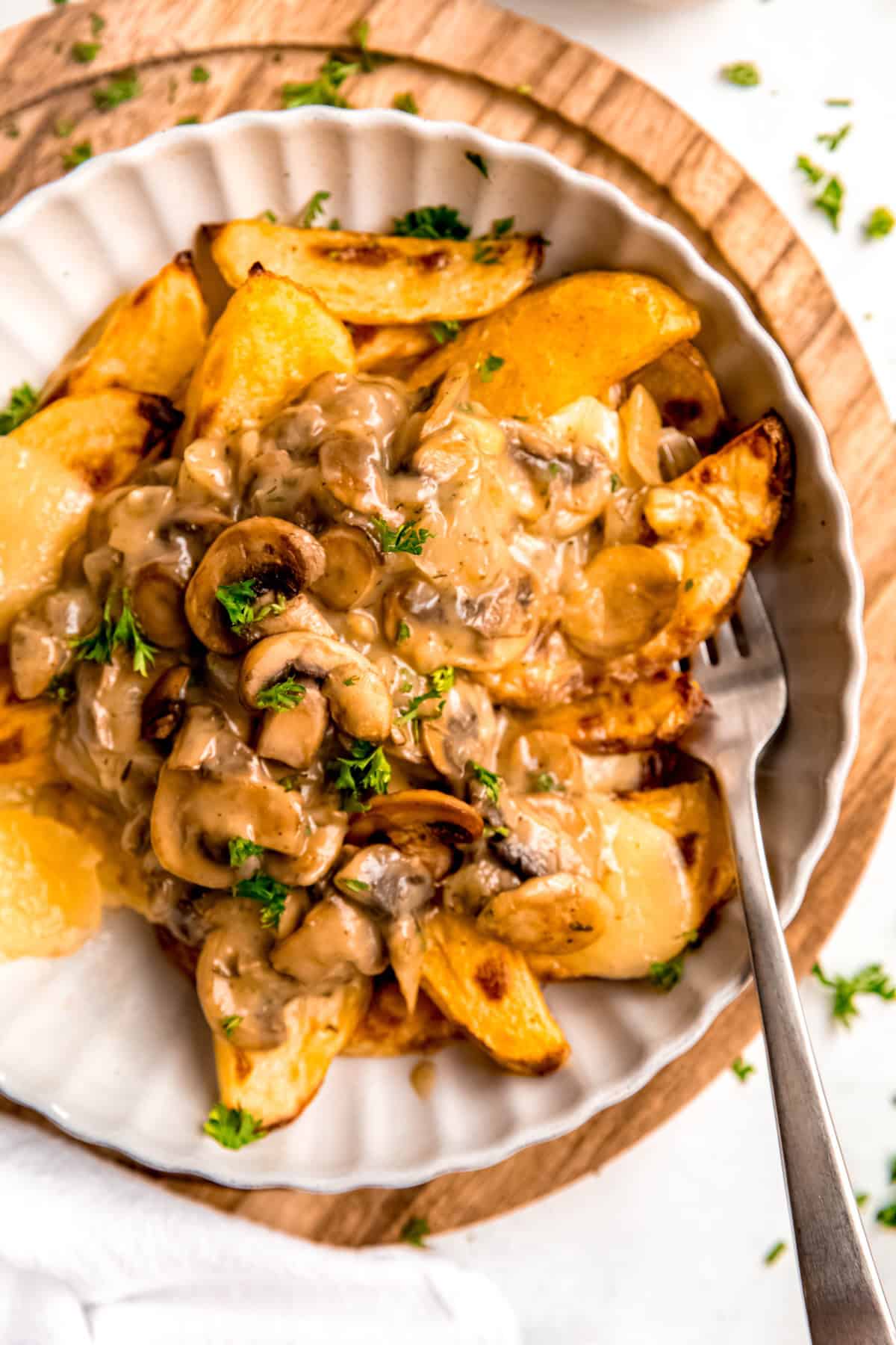 closeup overhead shot of a bowl of breakfast poutine with a silver fork stabbing a bite with a crispy potato wedge, cheese curd, and slice of mushroom from the gravy.