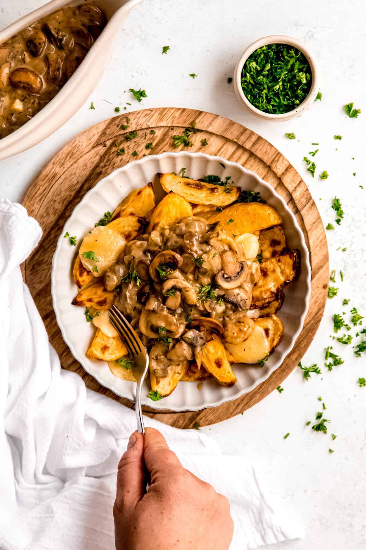 hand using a fork to stab a cheese curd and crispy potato wedge from a bowl of breakfast poutine.