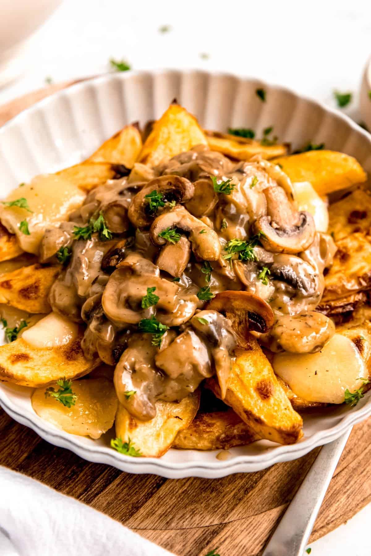 45 degree angle of a white bowl of brunch poutine on a wooden tray with a silver fork.
