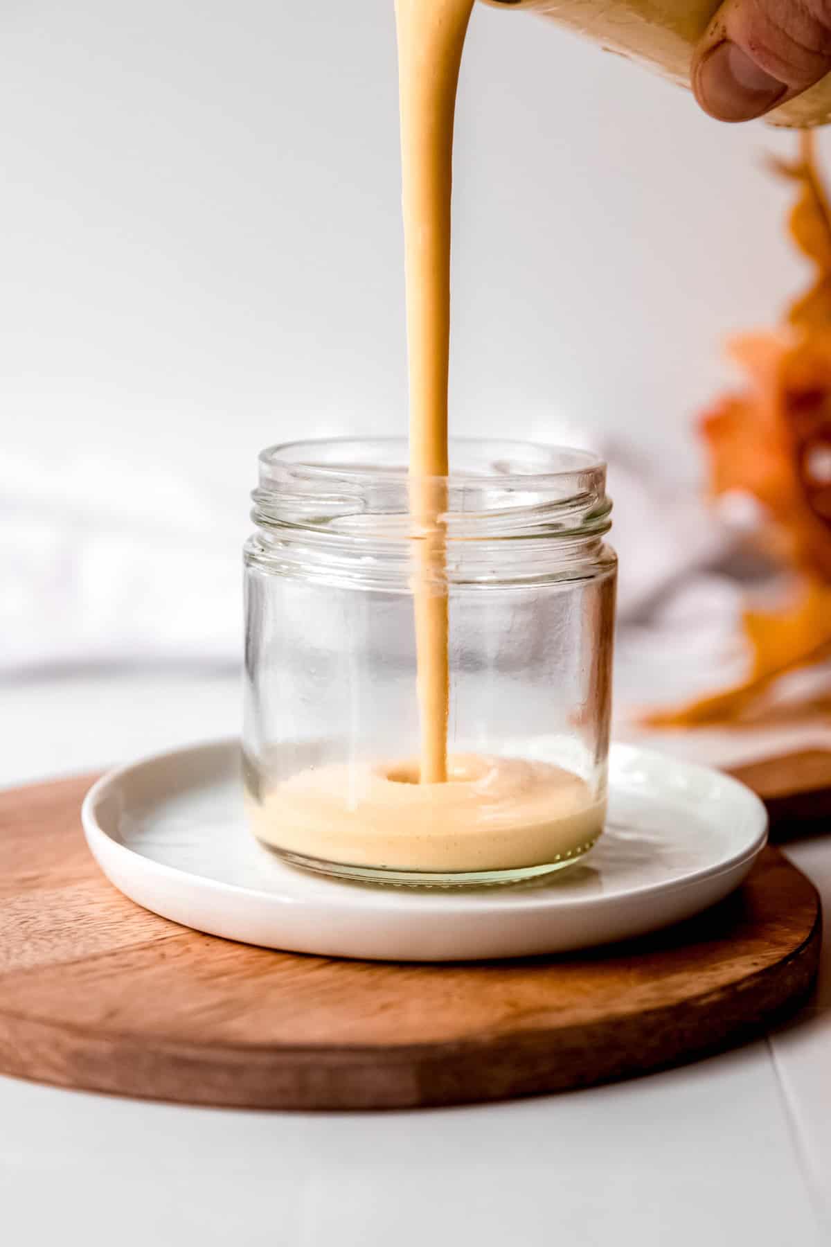 action shot of a hand pouring the freshly blended creamy maple dressing into a short glass jar.