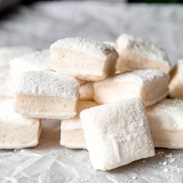 jumbled stack of fluffy vanilla marshmallows showing the vanilla bean-flecked interior and the powdered sugar exterior.