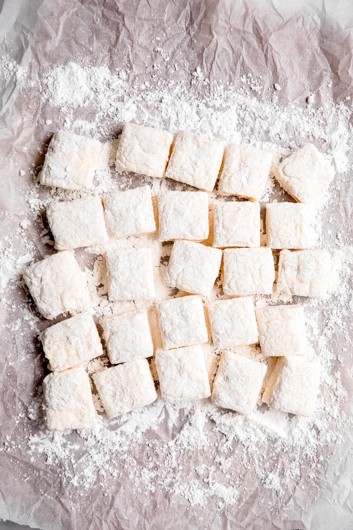 homemade marshmallows made with egg whites (and no dairy!) on a piece of crumpled parchment paper sprinkled with a mixture of powdered sugar and cornstarch.