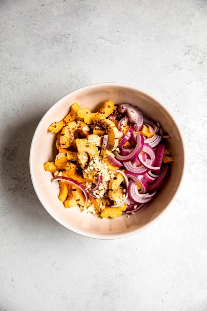 raw red onions, delicata squash, and garlic in a large bowl with olive oil and maple syrup before tossing and roasting.
