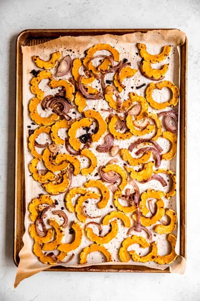roasted half moons of delicata squash and sliced red onion on a parchment lined baking sheet.
