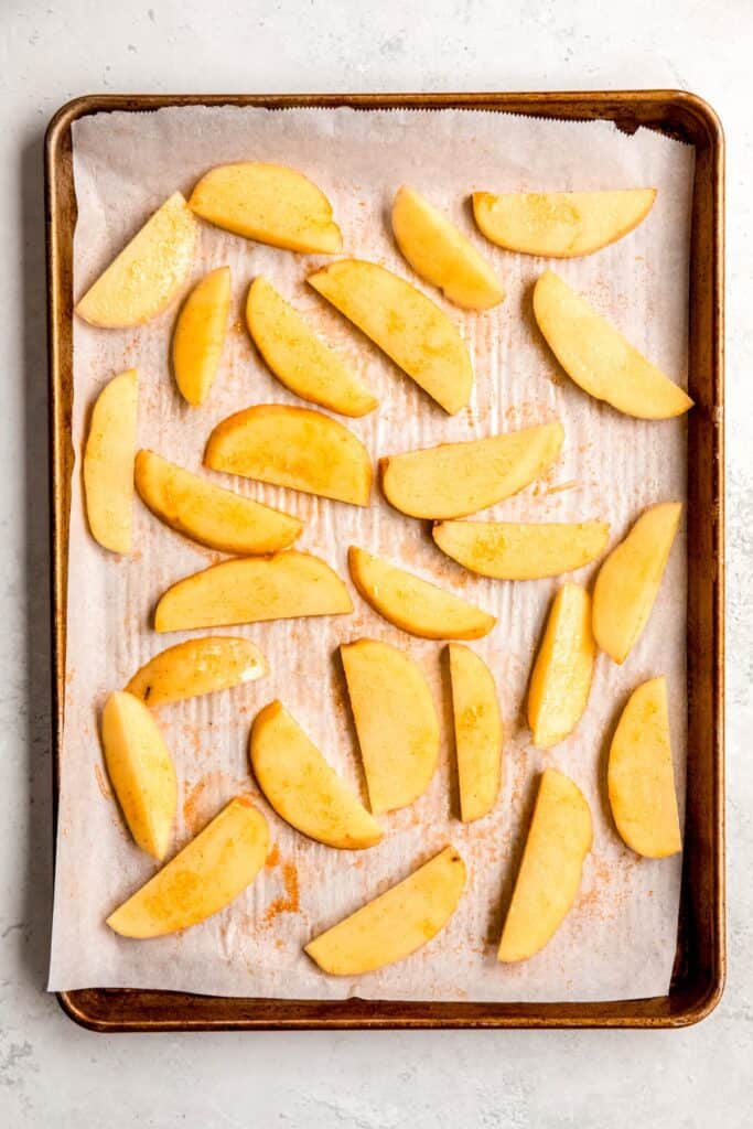 raw seasoned potato wedges spread out on a sheet pan lined with parchment.