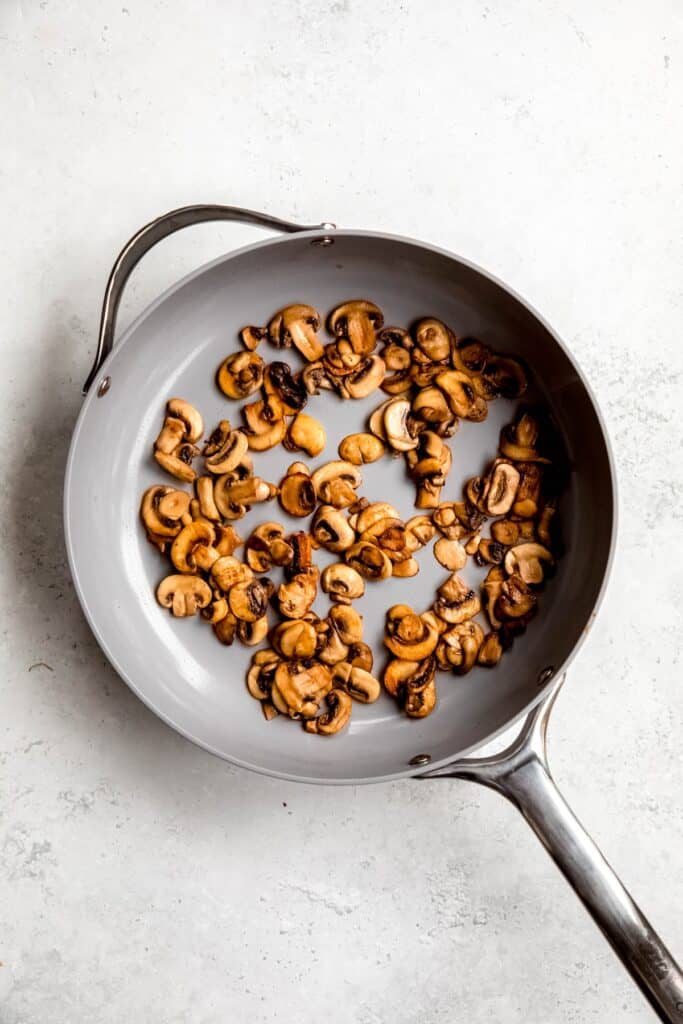 sliced mushrooms sautéing in a skillet.