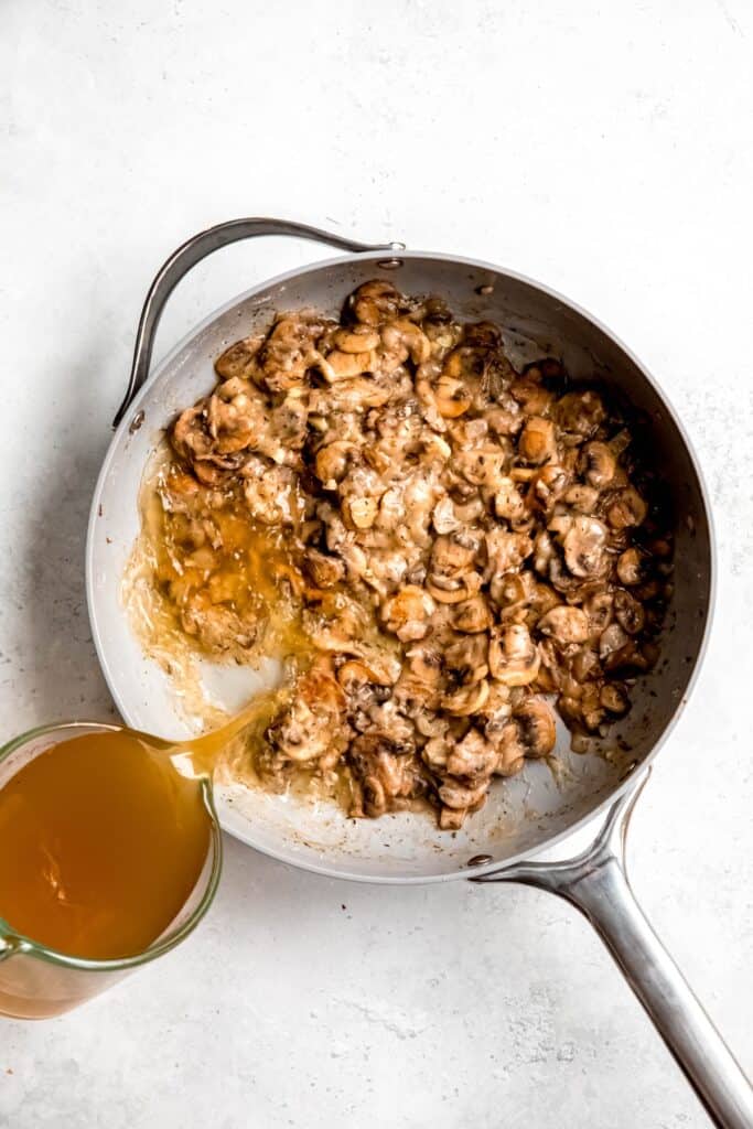 action shot of stock being added to the pan with the mushrooms and reduced wine.