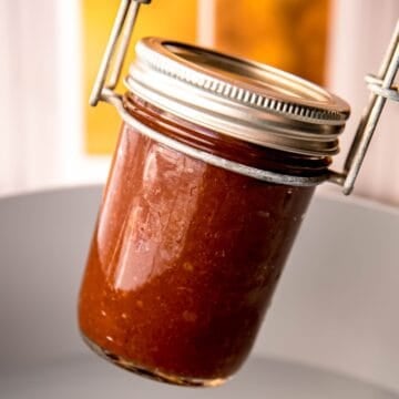 square hero shot of instant pot apple butter for canning being lowered into a hot water bath for processing.