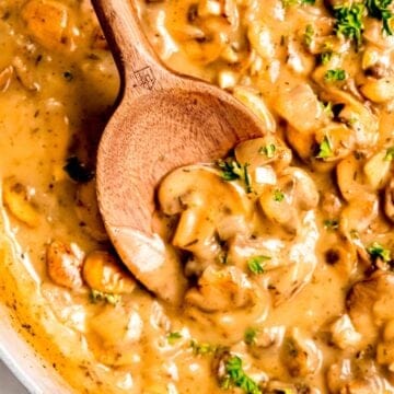 wooden spoon halfway in a skillet of creamy make ahead mushroom gravy to show how thick and glossy it is.