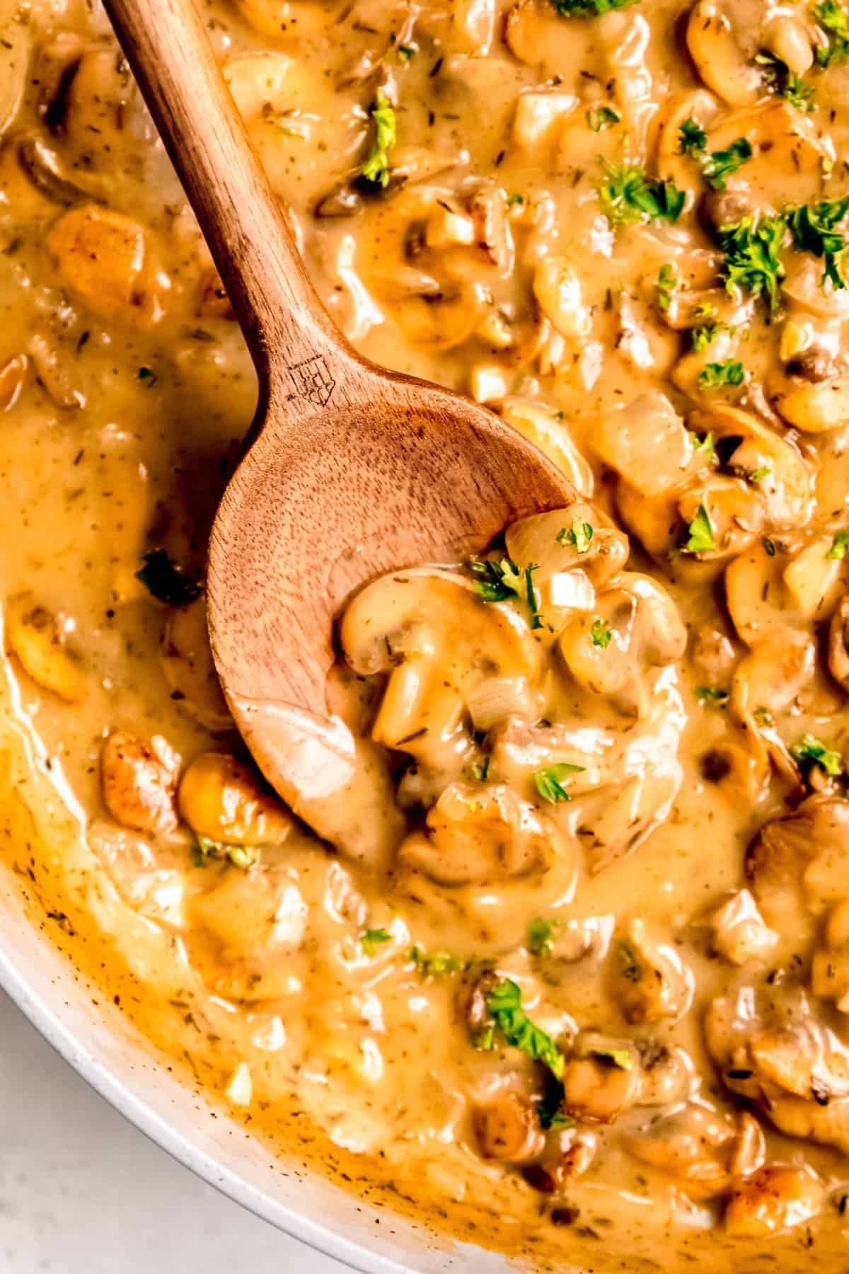 wooden spoon halfway in a skillet of creamy make ahead mushroom gravy to show how thick and glossy it is.