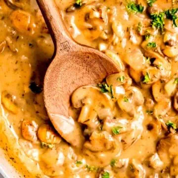 hyper closeup overhead square image of a wooden spoon in a saucepan of make ahead mushroom gravy.