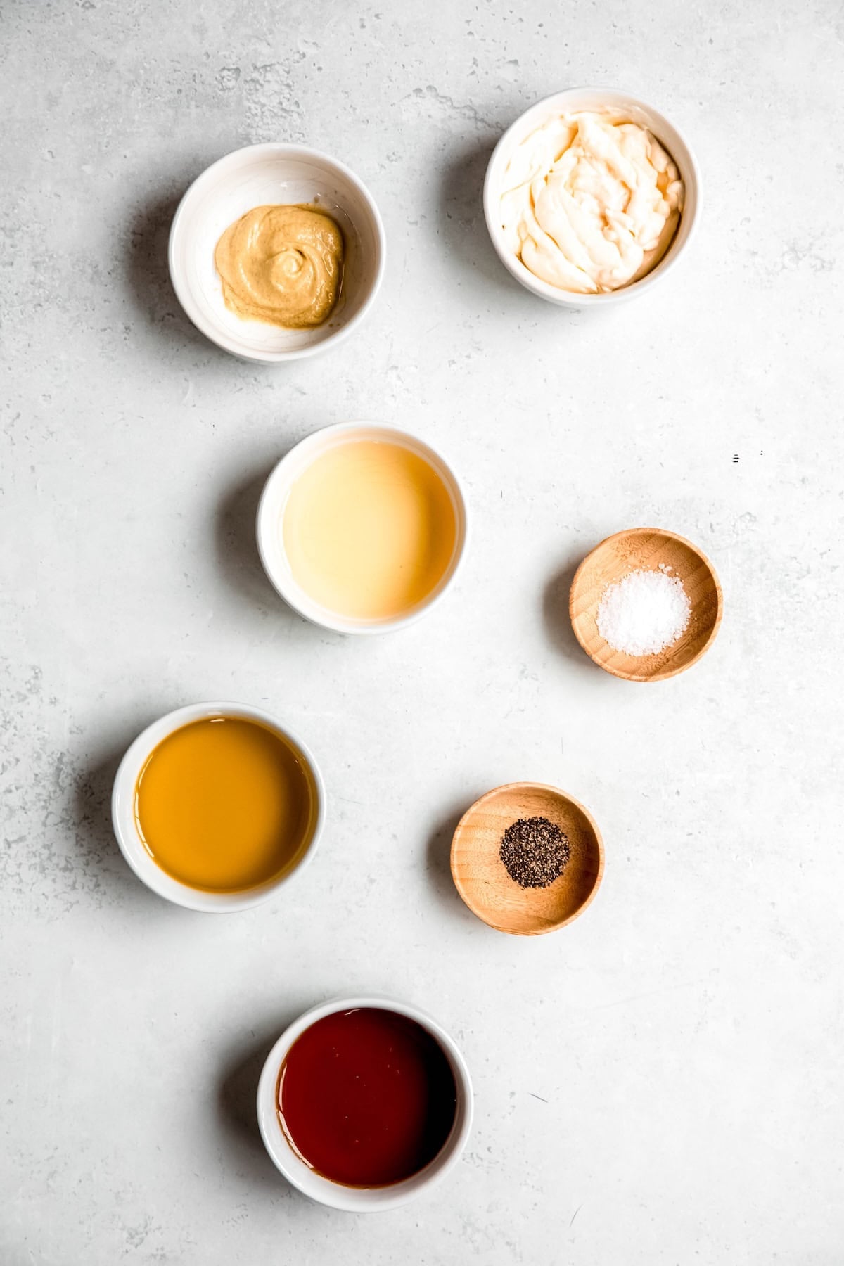 ingredients needed to make creamy maple dijon dressing measured out into bowls on a greyish white table.
