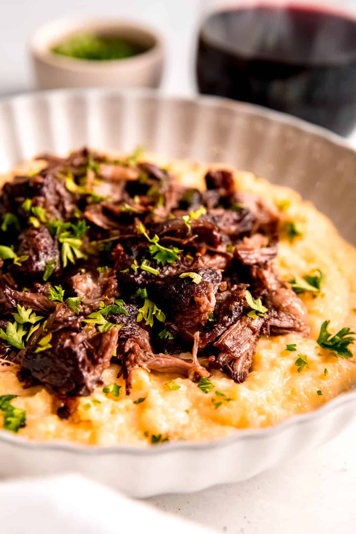 beef short ribs braised in red wine and served over a bowl of creamy parmesan polenta with a sprinkle of fresh parsley for garnish.