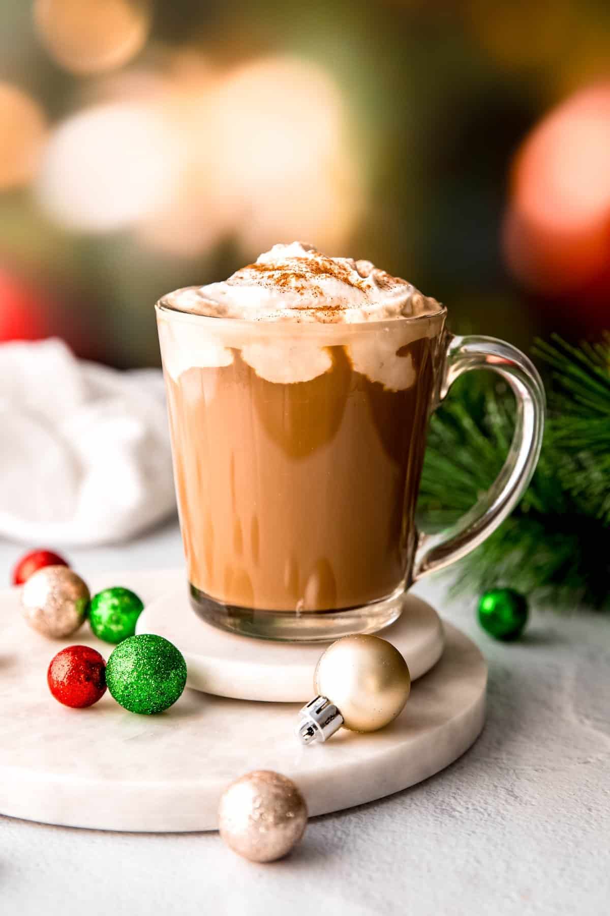 side on view of a festive christmas coffee spiked with irish cream, vodka, and kahlua and topped with amaretto whipped cream on a white table with christmas decorations.