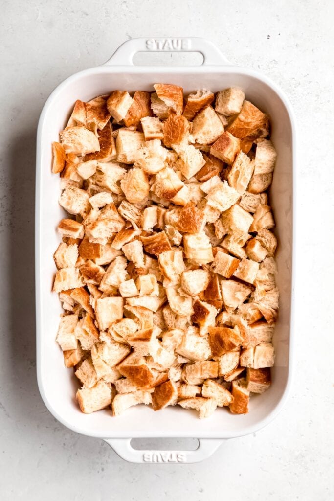 cubed croissants layered in the bottom of a white staub 9x13 casserole dish.