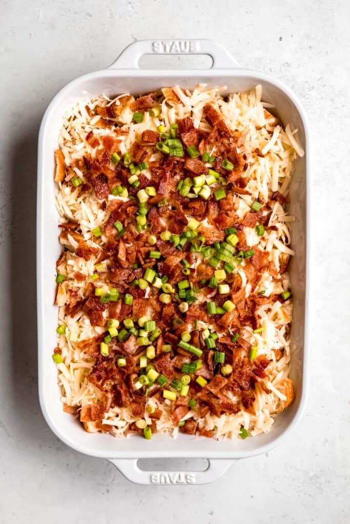overhead shot of the layered croissant breakfast casserole topped with cheese, bacon, and scallions.