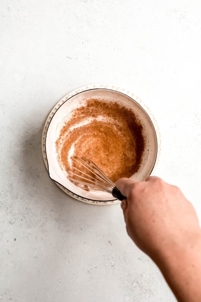 action shot of a hand whisking the milk mixture after adding the spices.