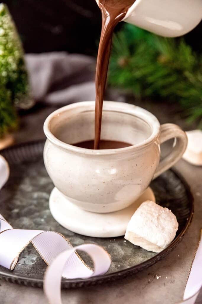 action shot of thick spicy Aztec hot chocolate being poured from the saucepan into a white ceramic mug.