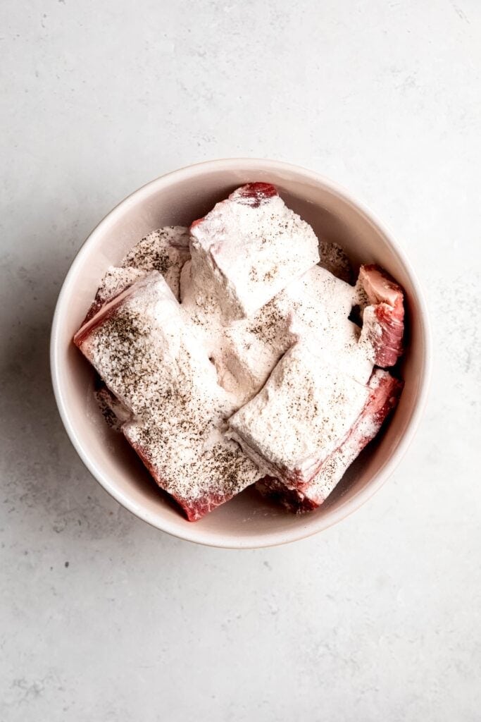 raw short ribs in a bowl with flour, salt, and pepper.