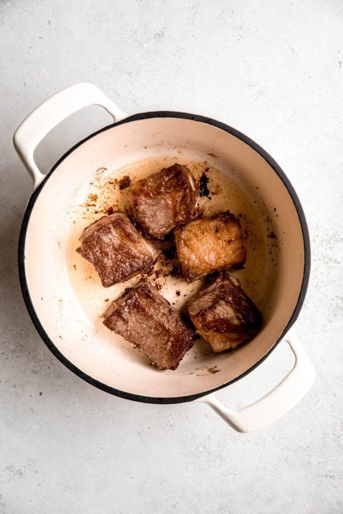 flour coated short ribs being browned in a dutch oven with oil before braising.