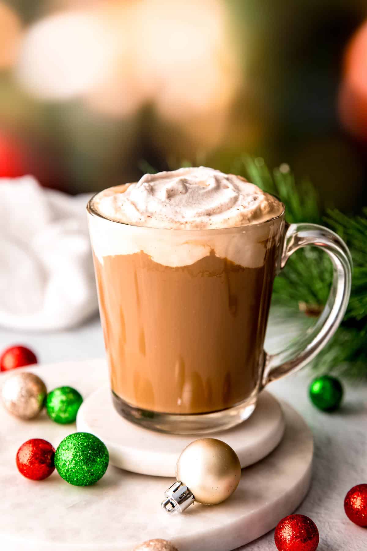 clear mug of merry christmas coffee on a festively adorned white table.