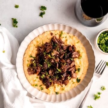square hero image of red wine braised short ribs over creamy parmesan polenta topped with fresh parsley.