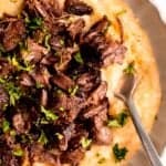closeup overhead shot of a plate of red wine short ribs with parmesan polenta; a silver fork is digging in for a bite.