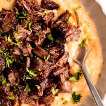 closeup overhead shot of a plate of red wine short ribs with parmesan polenta; a silver fork is digging in for a bite.