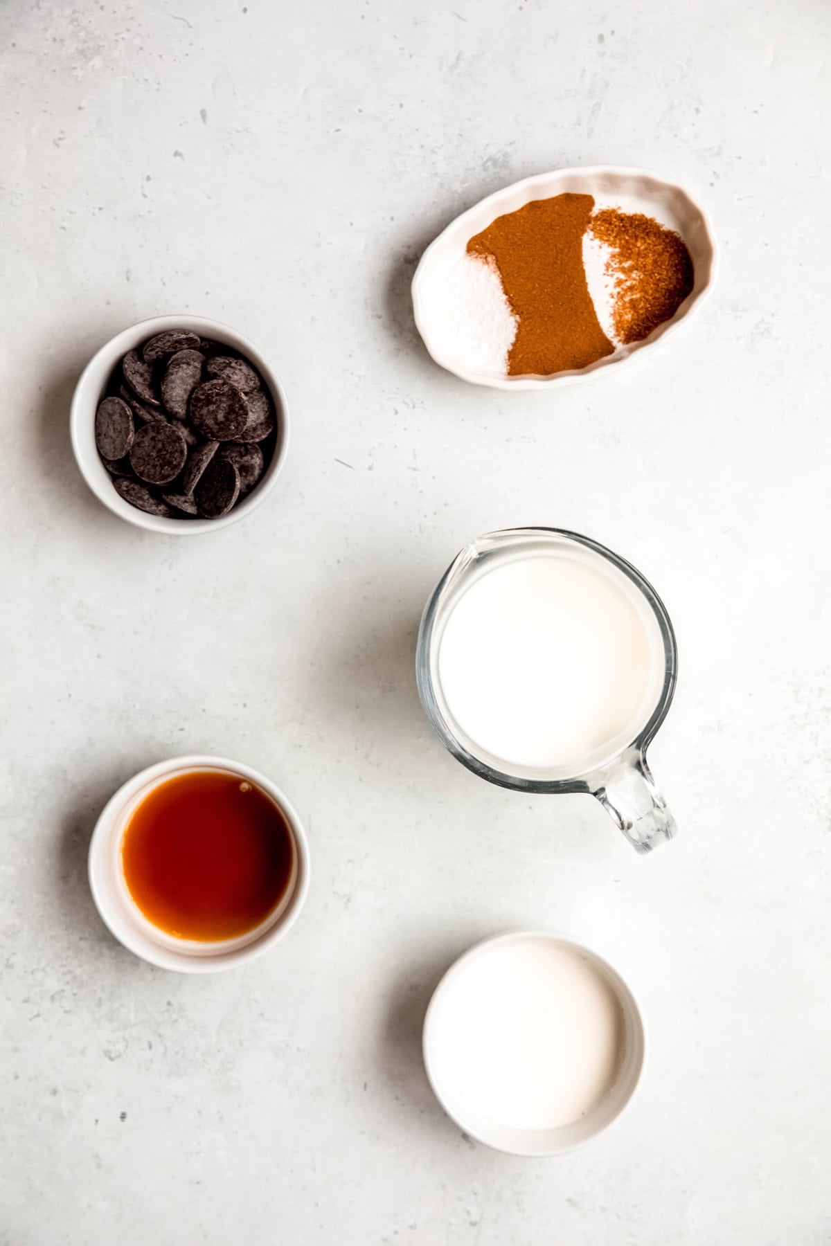 ingredients needed to make spicy aztec hot chocolate recipe measured out into white bowls on a white table.