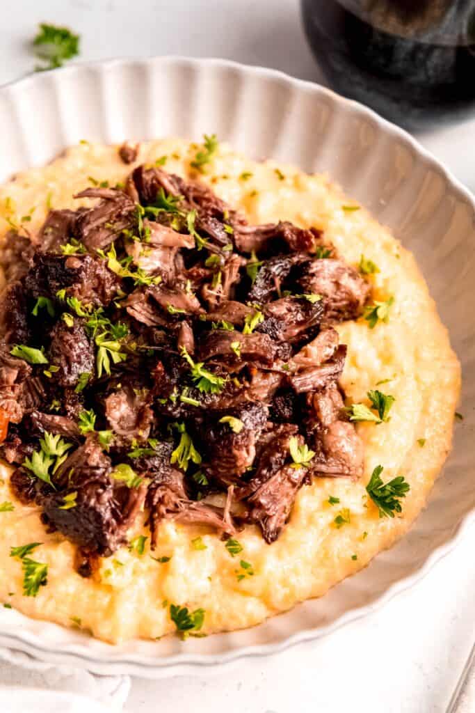 45 degree angle shot of a scalloped round white pasta bowl with parmesan polenta topped with red wine braised short ribs.