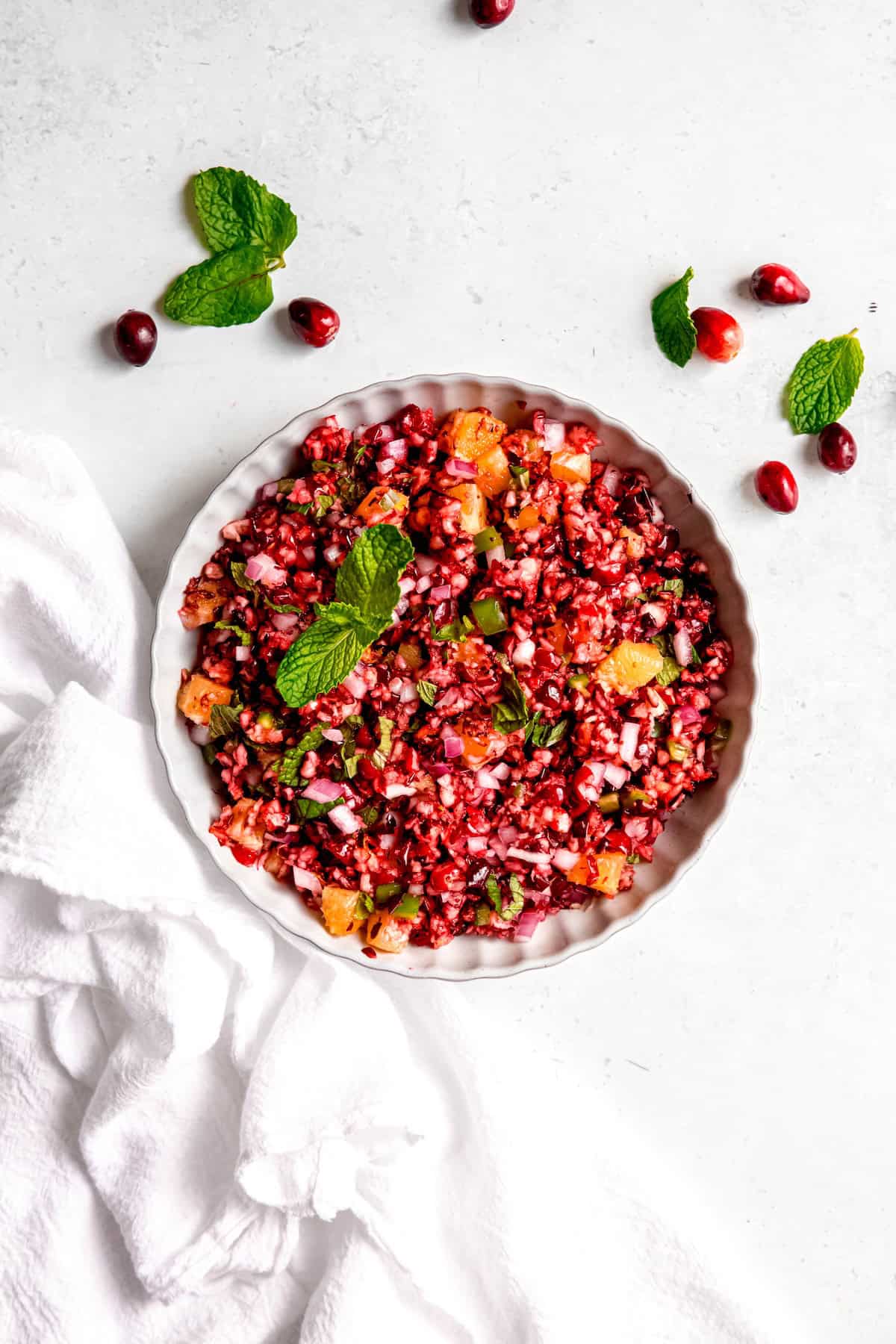 white serving bowl of fresh cranberry jalapeno dip with oranges and mint.