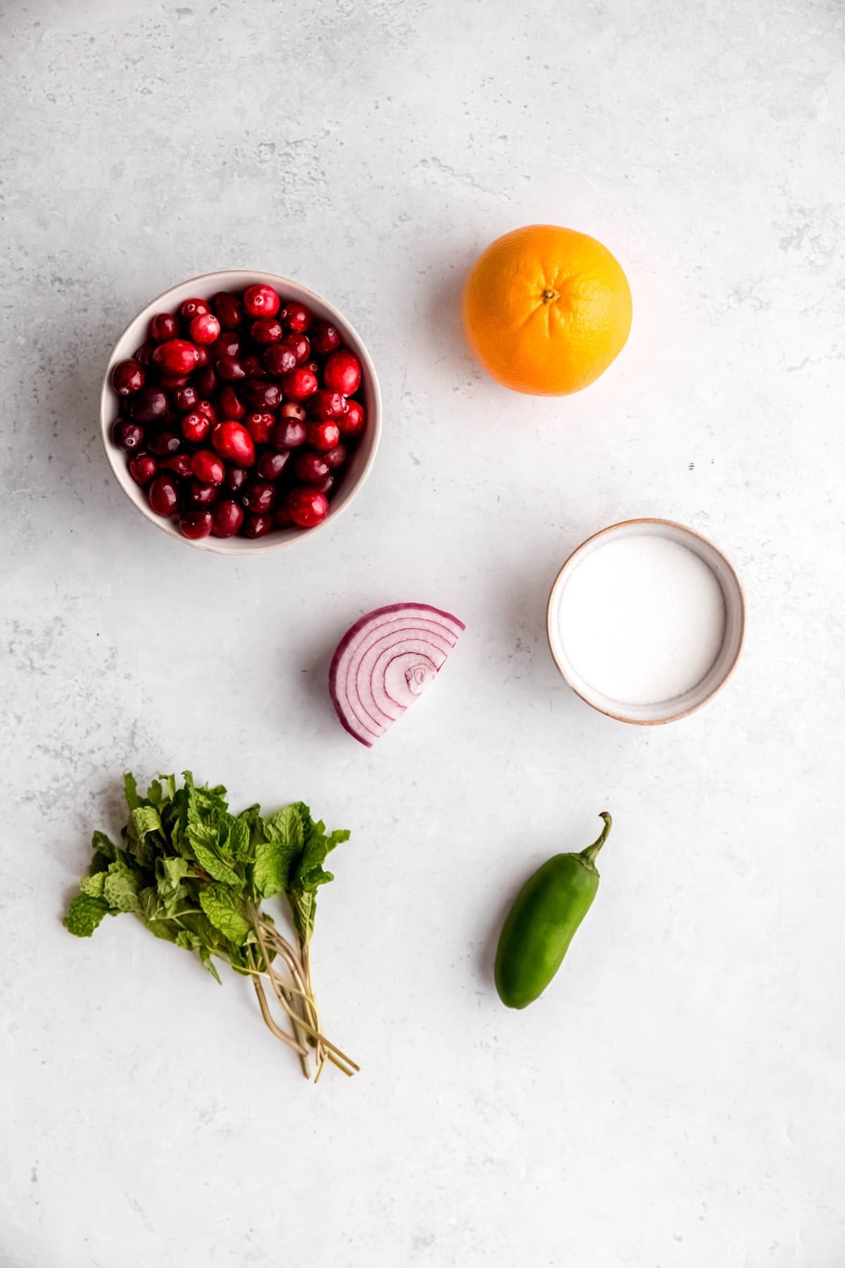 ingredients needed to make raw orange cranberry jalapeño relish recipe measured out on a white table.
