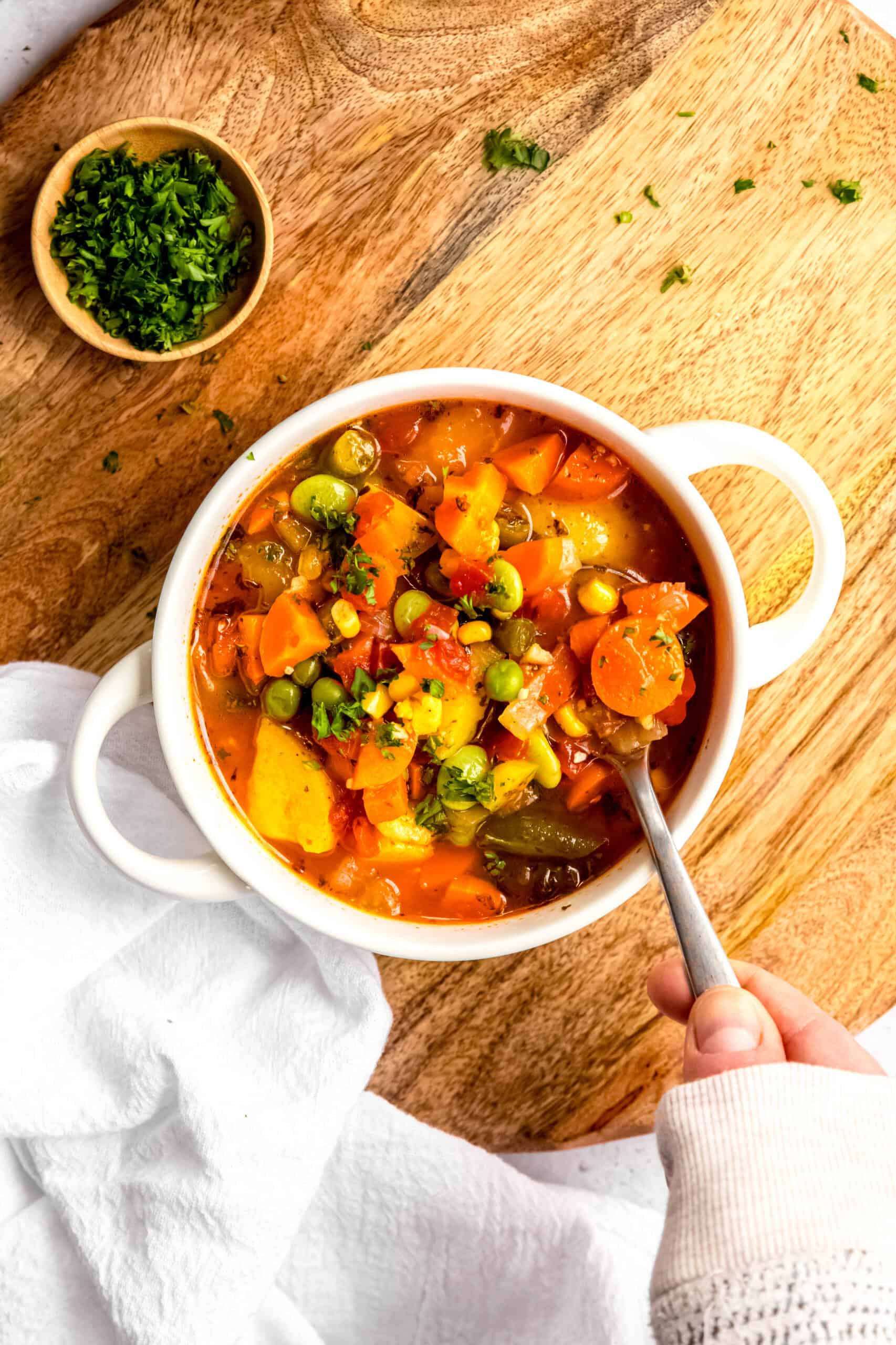 hand clad in a cozy white sweater up to the knuckles using a silver spoon to take a bite from a bowl of frozen vegetable instant pot soup.