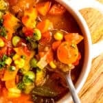 closeup of the right ¾ of a white bowl of instant pot vegetable soup with a silver spoon taking a spoonful, showing off the chunky veggies.