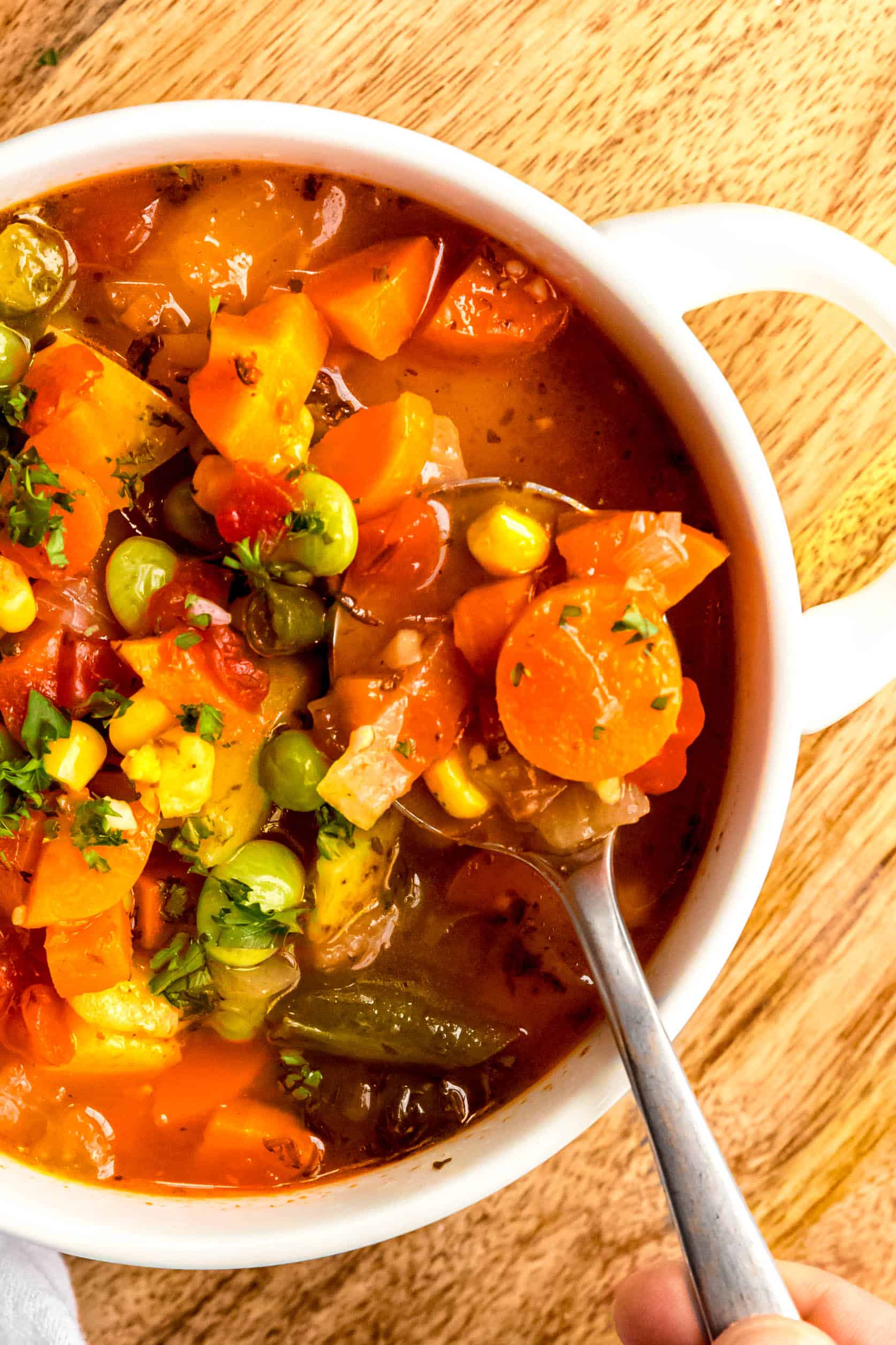 closeup of the right ¾ of a white bowl of instant pot vegetable soup with a silver spoon taking a spoonful, showing off the chunky veggies.