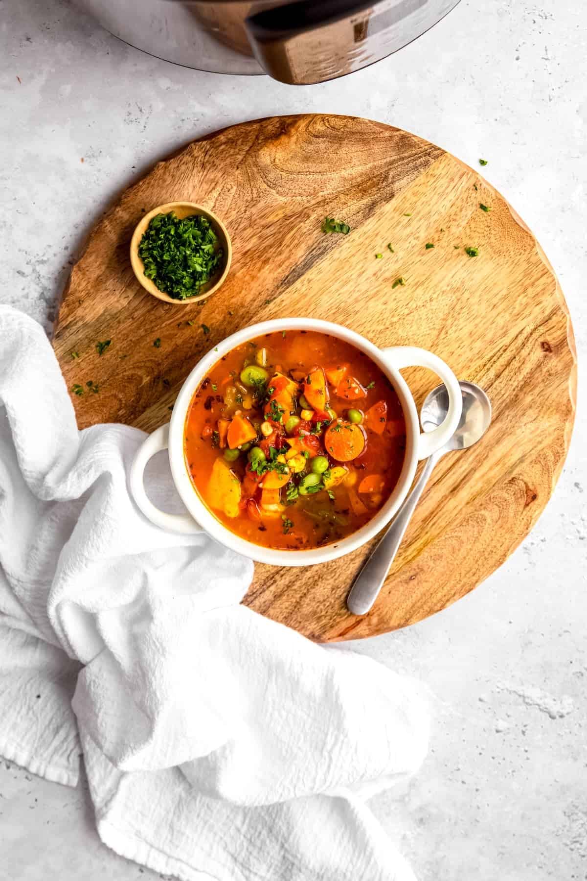 overhead shot of a serving of vegetable soup made with frozen veggies on a wooden trivet on a grey table with parsley sprinkled around and an instant pot in the top of the frame.