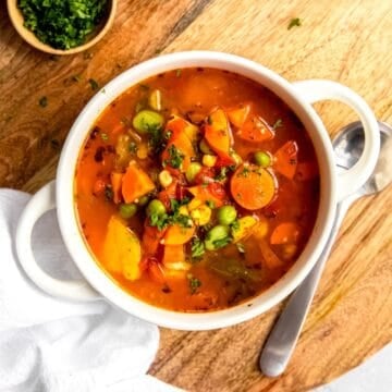 square hero closeup image of instant pot vegetable soup made with frozen vegetables in a white bowl with a sprinkle of fresh parsley.