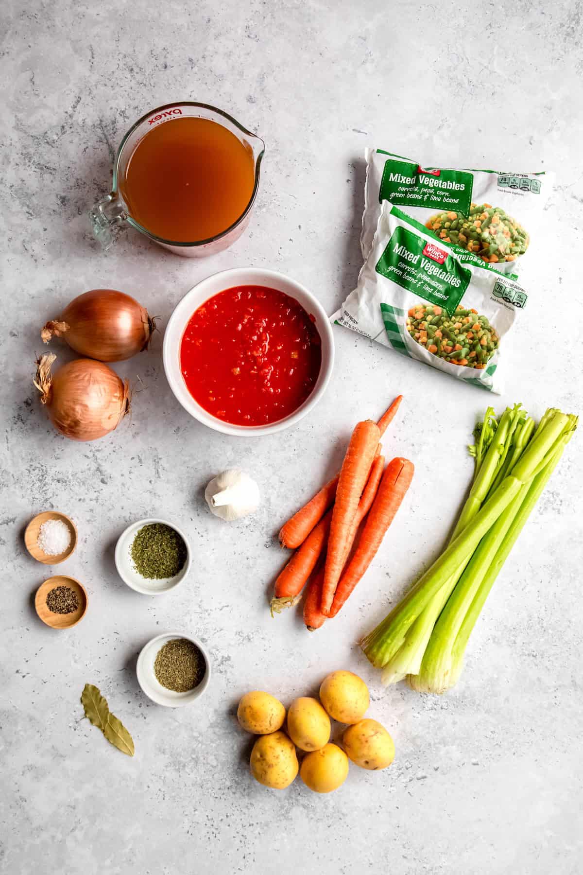 ingredients for vegetable soup recipe with frozen vegetables measured out on a grey table.