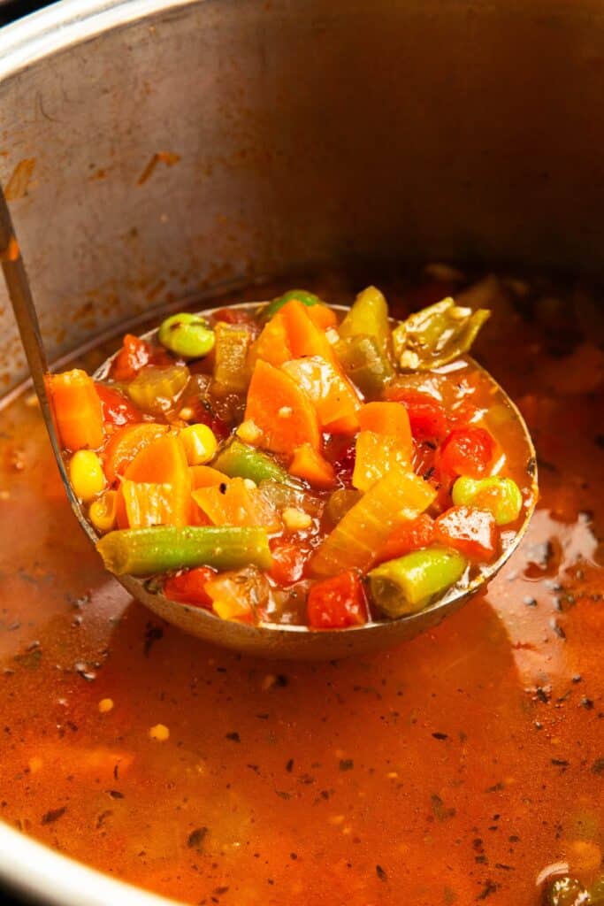 silver ladle taking a serving of veggie soup made with frozen vegetables from the insert of an instant pot.