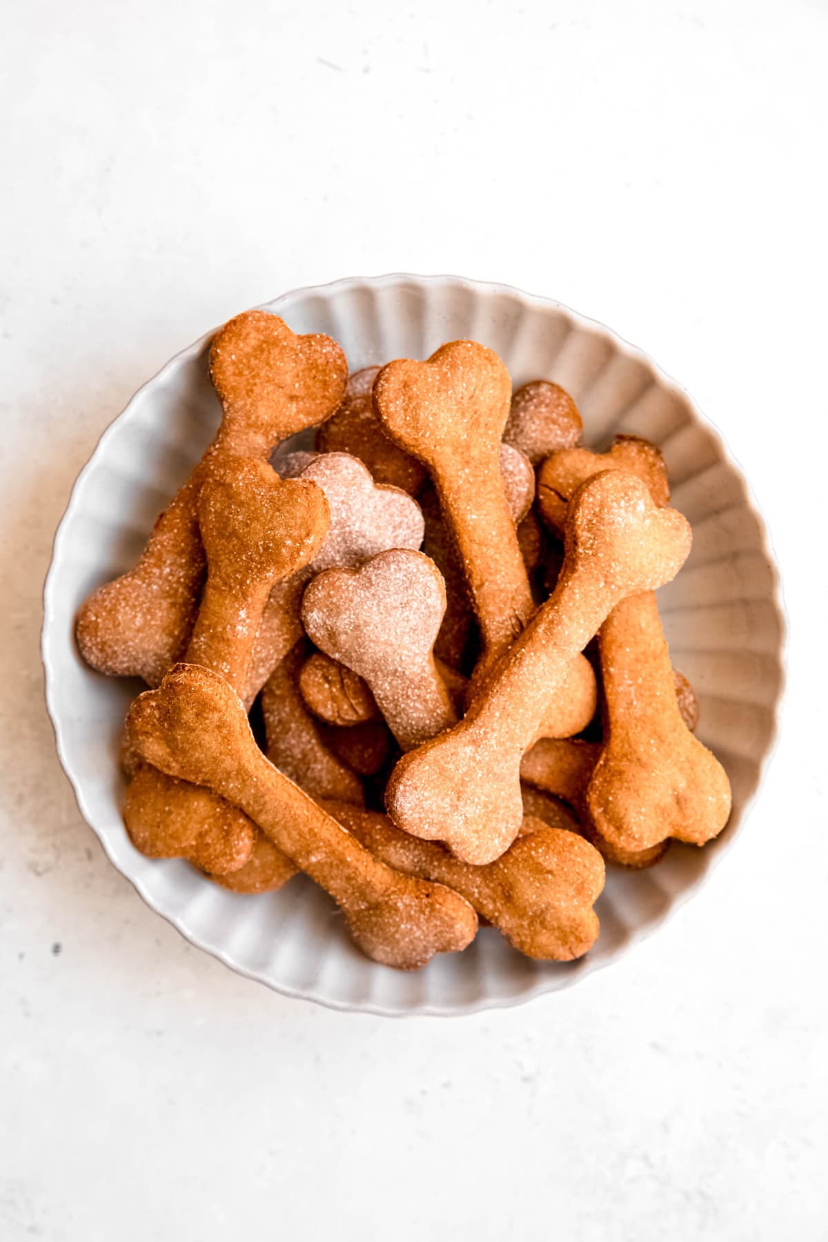overhead shot of a white bowl filled with banana peanut butter dog treats on a white table.