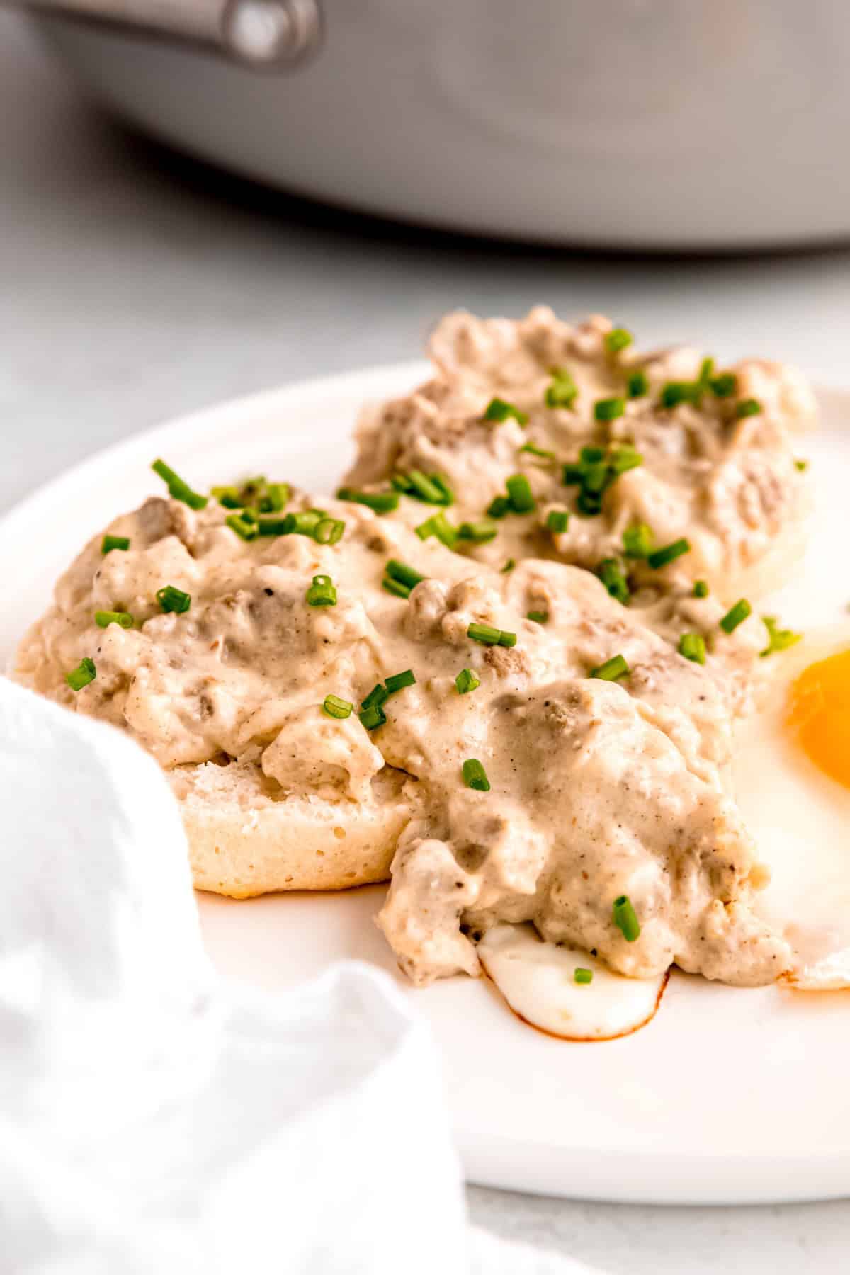 45 degree angle shot of a plate of biscuits with old fashioned sausage gravy and a fried egg topped with fresh chives.