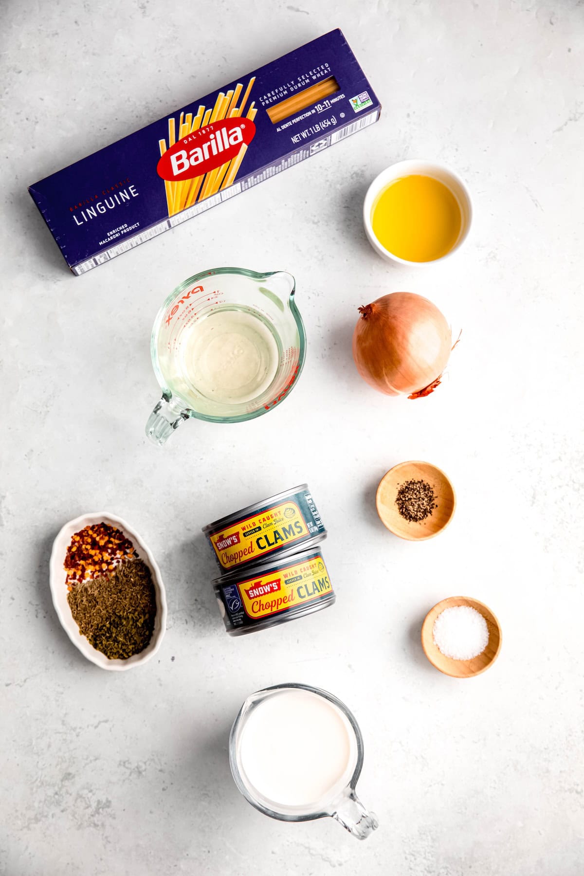 ingredients needed to make pantry-based canned clam linguine with white wine sauce measured out on a white table.